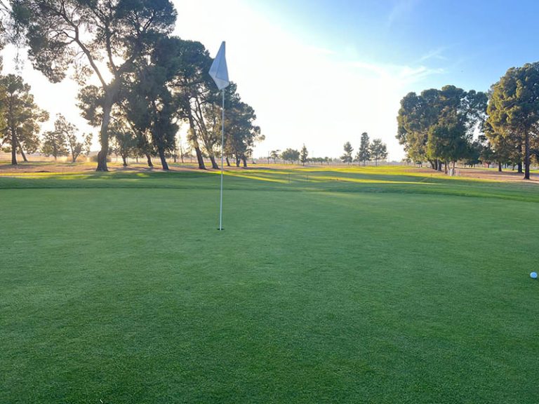Flagstick on a golf green at Airways Golf Course in warm late-day sunlight.