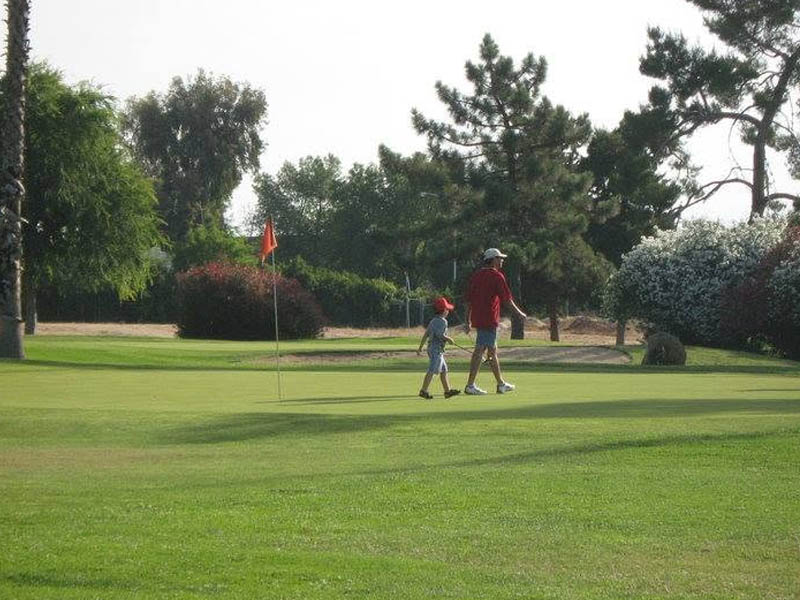 Golfers walking across a putting green near the flagstick at Airways Golf Course.