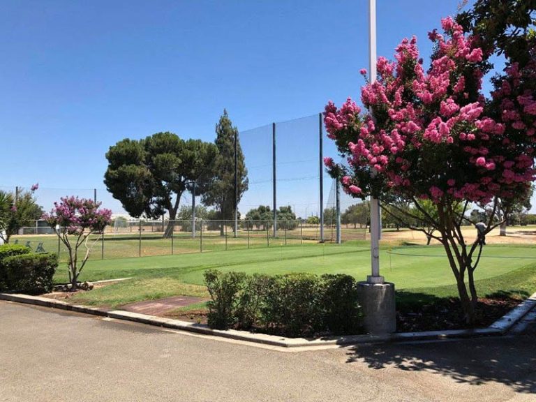 Landscaped golf course grounds with flowering trees, practice netting, and fairway views.